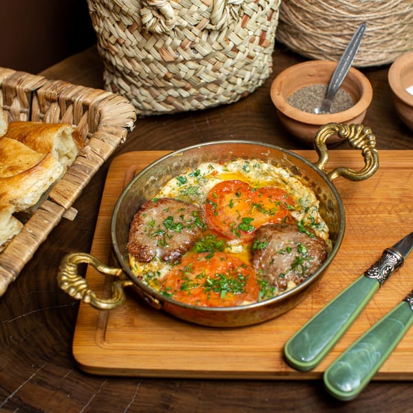 Mediterranean breakfast skillet with eggs, meatballs, tomatoes, and herbs, served with bread.