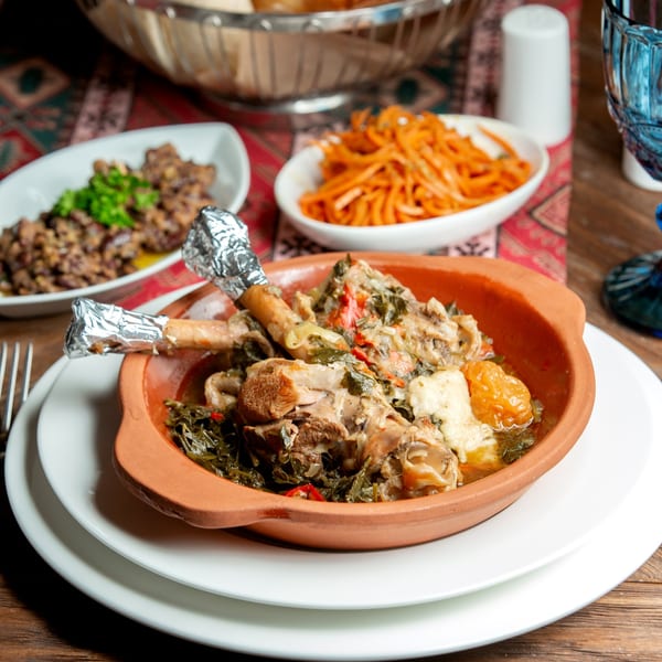 Mediterranean chicken stew with greens and apricots in a clay bowl, with sides of shredded carrots and minced meat.