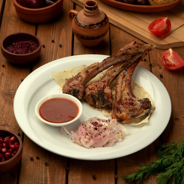 Grilled lamb chops with red sauce, sliced onions, and flatbread on a white plate.