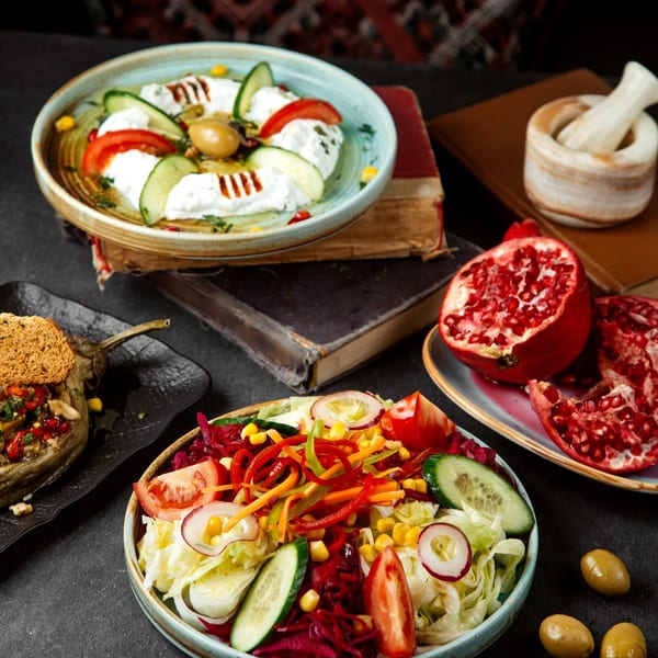 A Mediterranean spread featuring a fresh salad, yogurt dip, stuffed eggplant, and pomegranates.